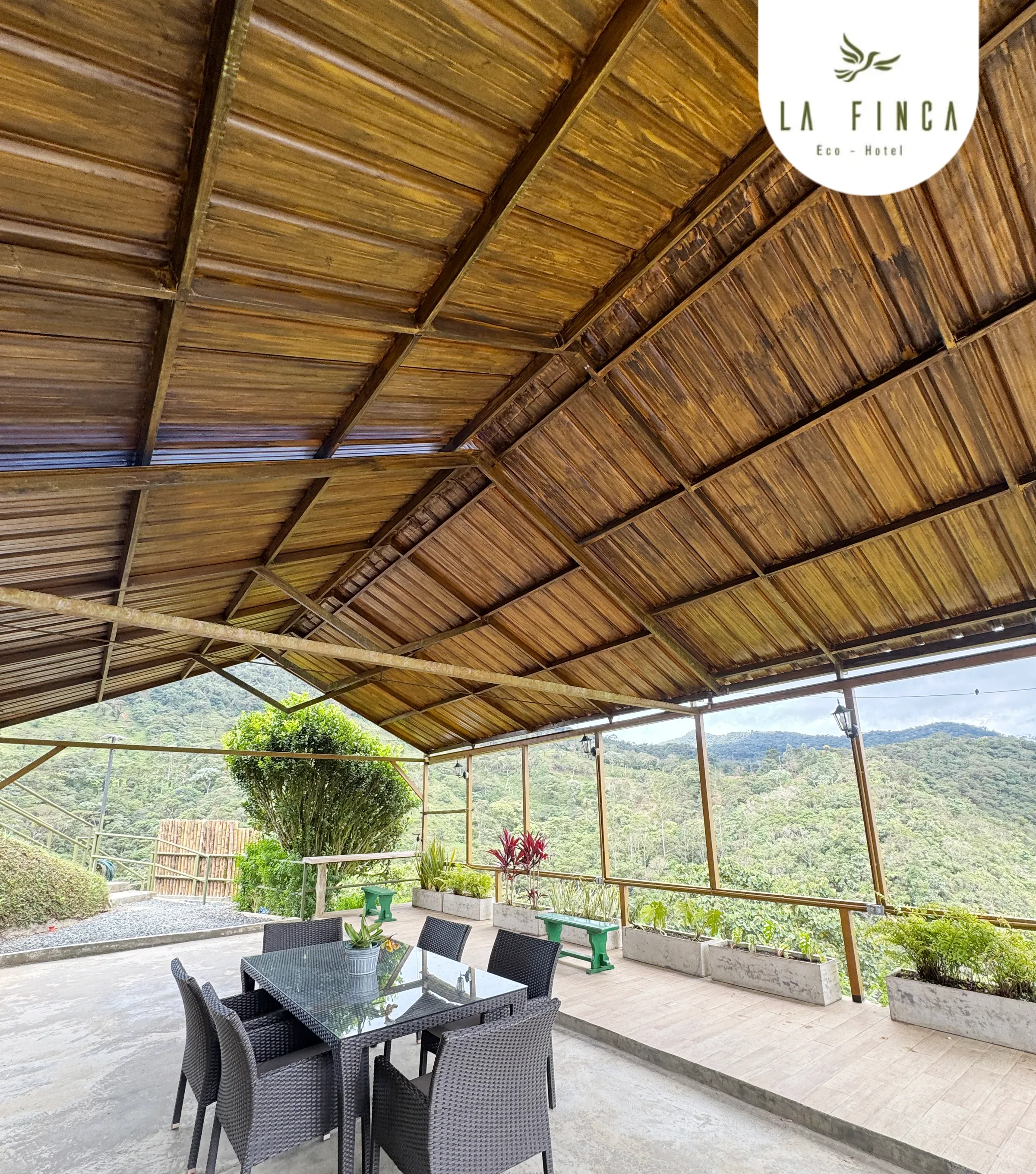 Deck techado de La Finca con comedor de vidrio y sillas, frente a las montañas