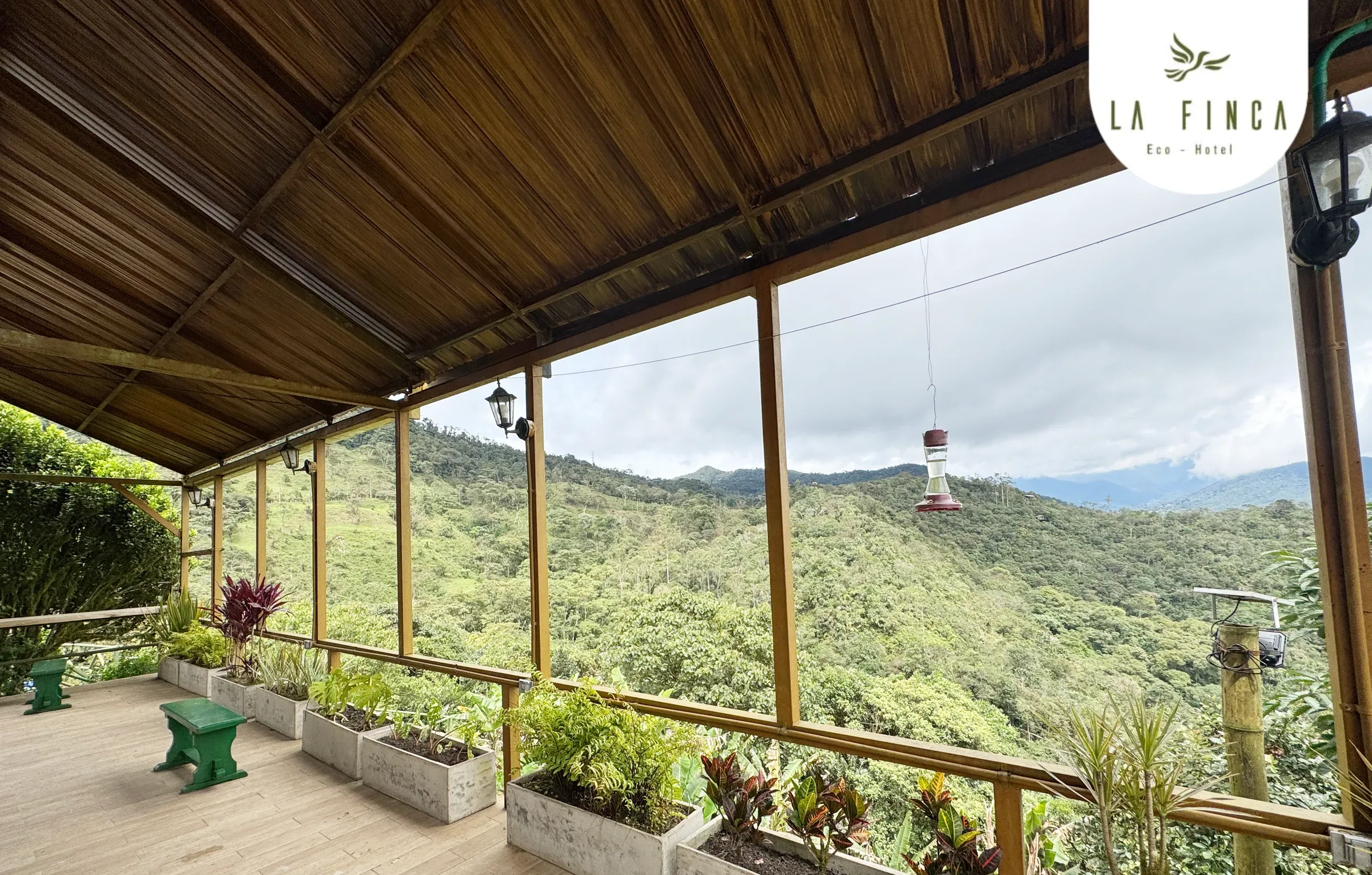 Corredor techado de La Finca con jardineras y baranda de madera, abierto al bosque de niebla del Km 18