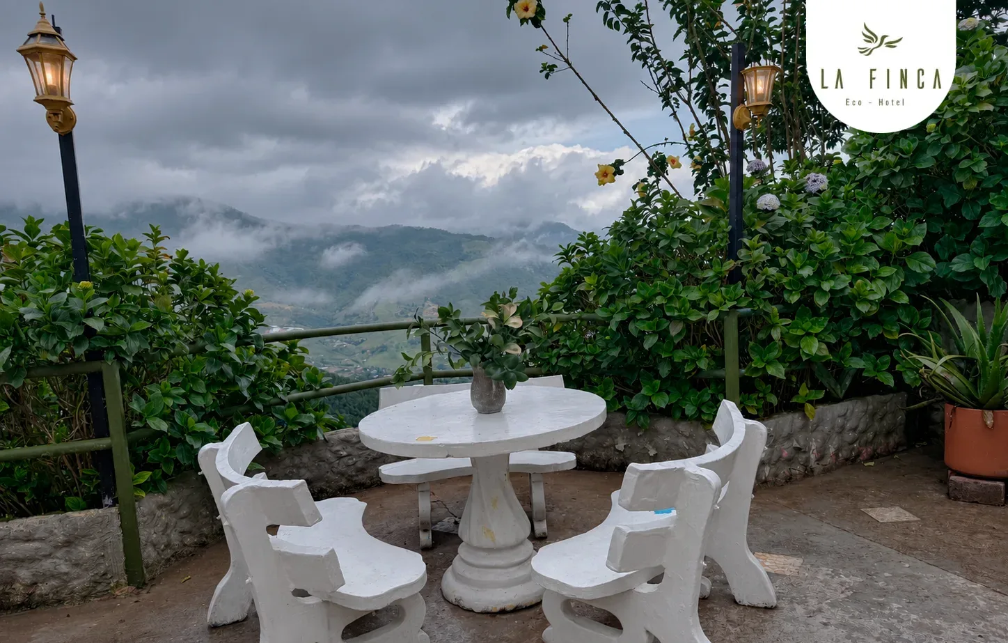 Mesa y sillas de piedra bajo las farolas de La Finca Eco Hotel, entre la neblina del atardecer