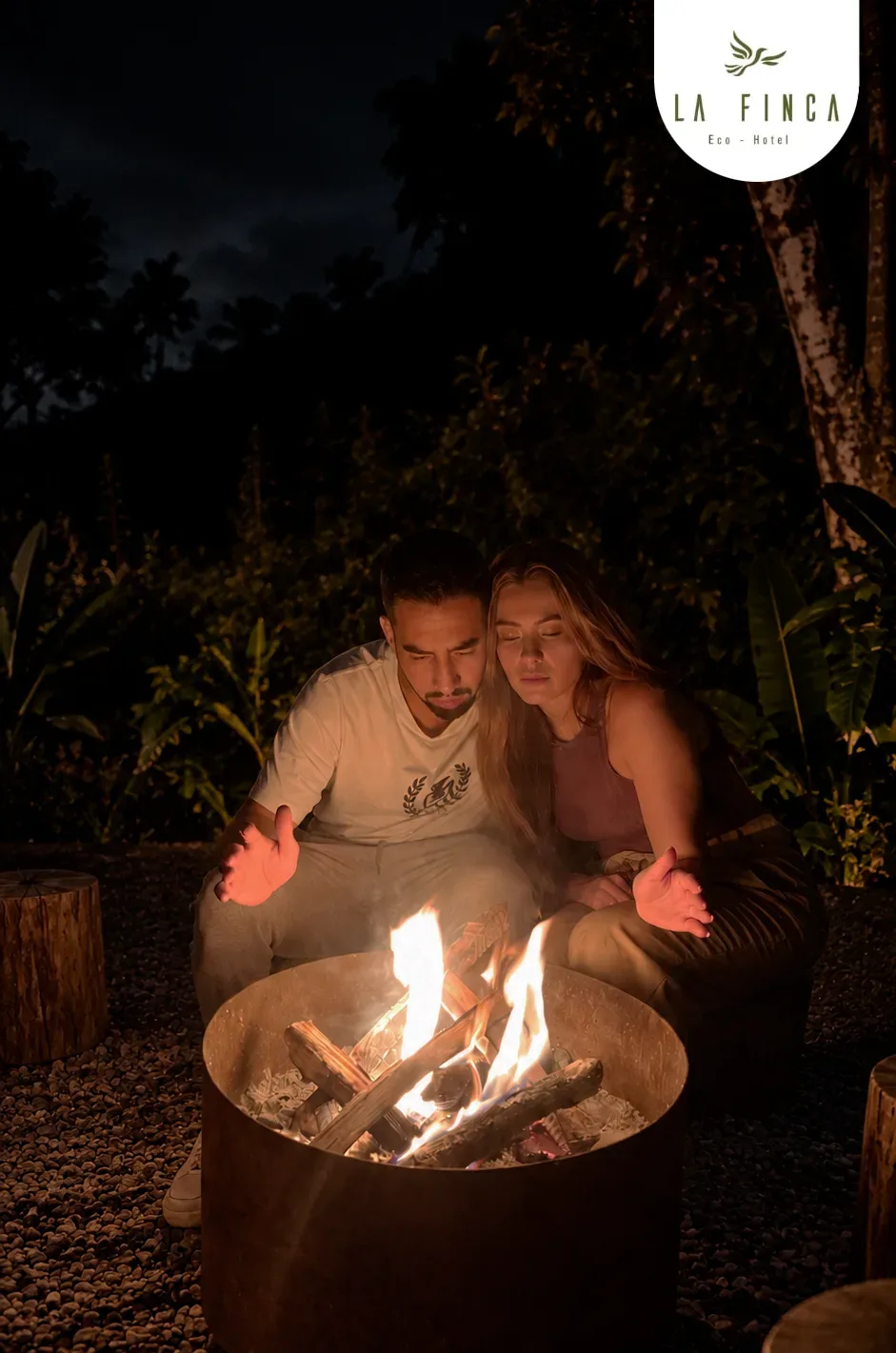 Pareja abrigada frente a la fogata encendida de La Finca, de noche